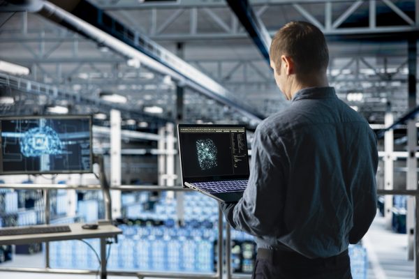 Data center IT specialist monitoring AI LLM visualization output to verify inference patterns. Programmer analyzing neural language network structure in server room using laptop
